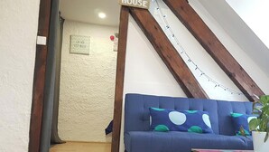 Ein gemütliches Wohnzimmer mit einem blauen Sofa, einem Couchtisch und einer Zimmerpflanze. Ein Schild weist darauf hin, dass es sich um ein 'Beach House' handelt.