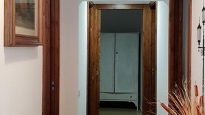 Un pasillo con piso de madera, un cuadro enmarcado a la izquierda, un marco de puerta de madera a la derecha y una lámpara en el techo.