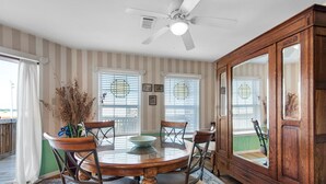 Une salle à manger avec une table ronde en bois, quatre chaises, un ventilateur de plafond et un grand meuble-miroir.