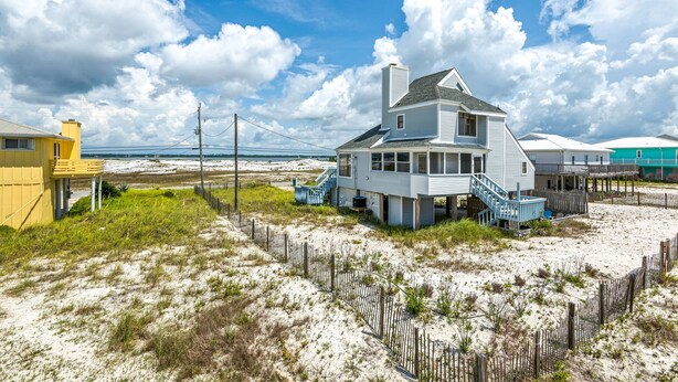 Une maison située sur la côte, avec un escalier menant à l’entrée principale, entourée de dunes de sable et d’une clôture en bois.