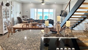 A spacious living area with a large dining table, comfortable seating, and a view of the ocean.