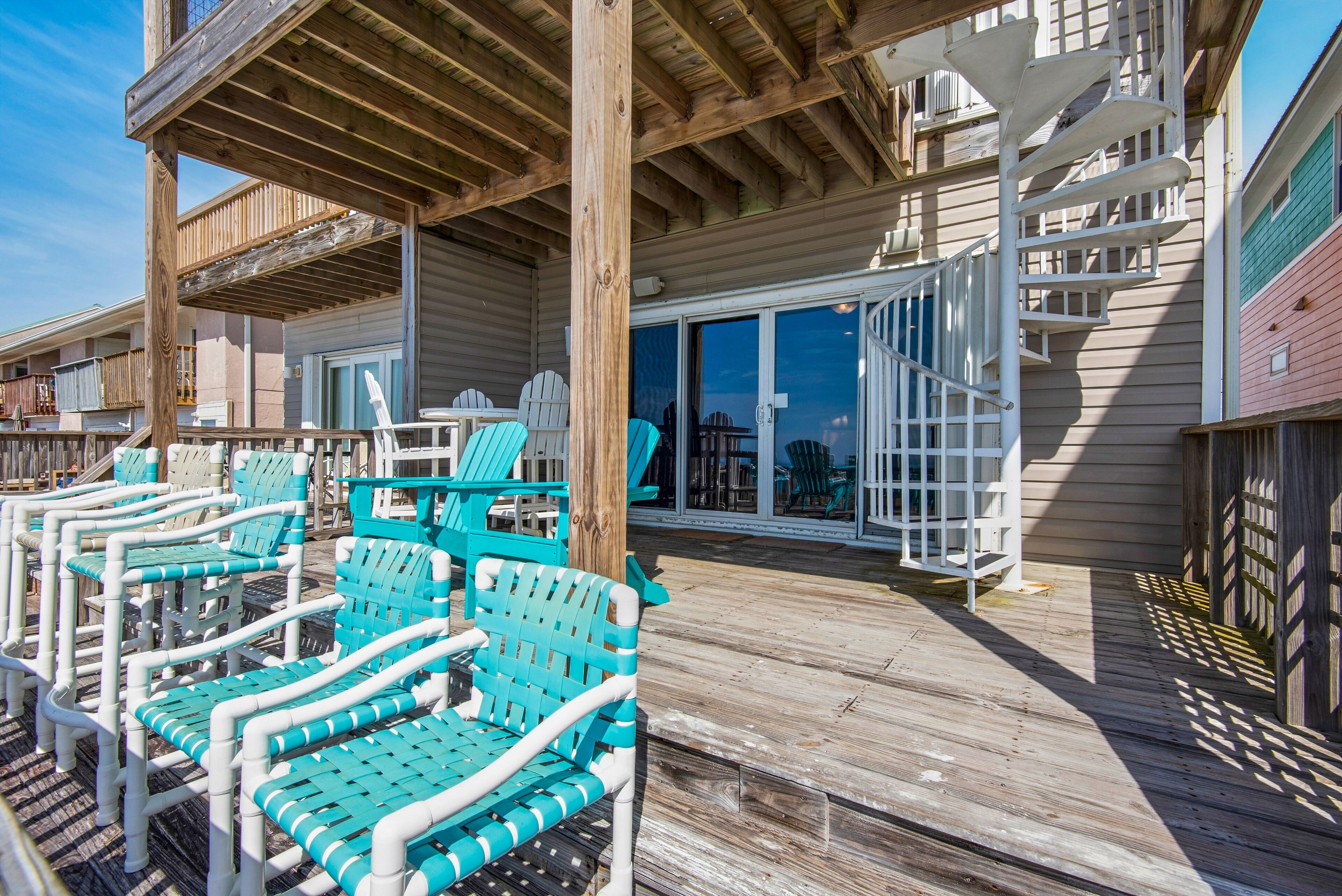 A wooden deck with turquoise Adirondack chairs and a white railing.