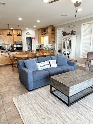 A modern kitchen with wooden cabinets, a dining area with a blue sofa, and a wooden coffee table.