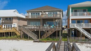 A beachfront property with a wooden deck leading to a house with multiple balconies and a covered outdoor area.