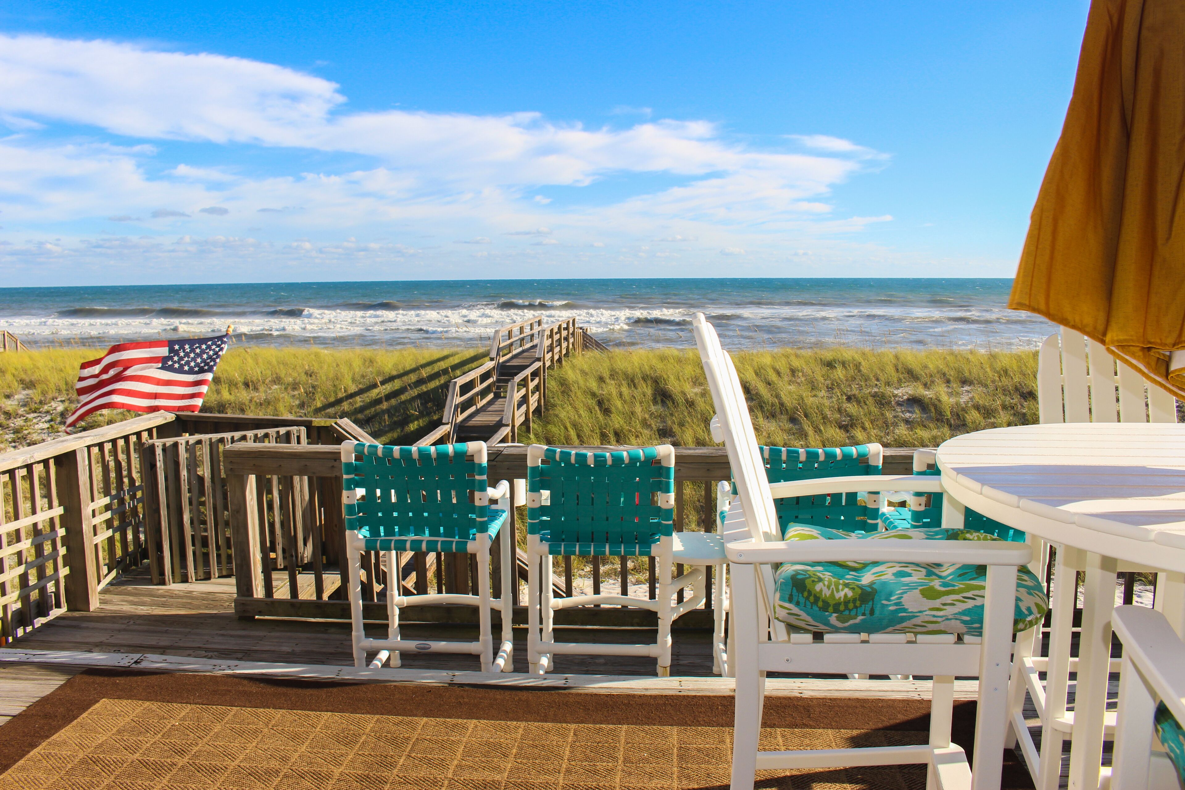 A wooden deck with chairs and a table, overlooking the ocean.