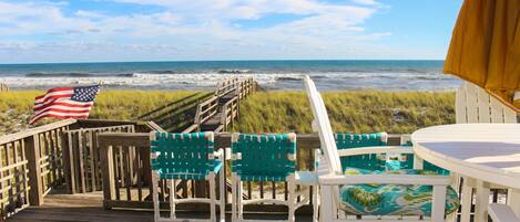 A wooden deck with chairs and a table, overlooking the ocean.
