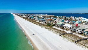 An aerial view of a coastal area with a beach, buildings, and a clear blue sky.