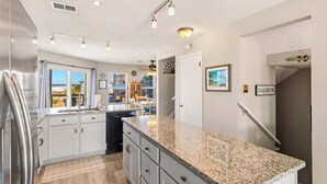 A modern kitchen with granite countertops, white cabinetry, and a view to the outside. - Pelican Roost 2 Bedroom Townhouse by RedAwning (Navarre)