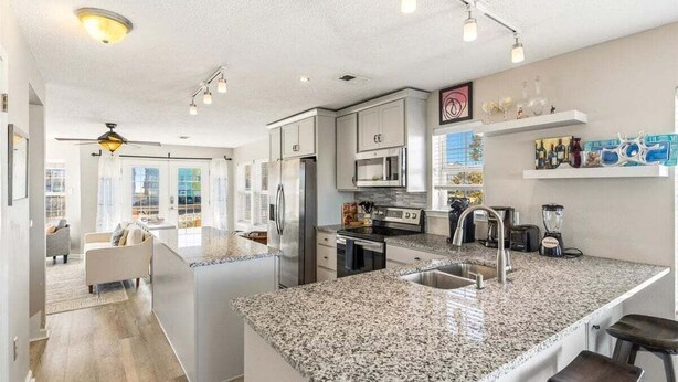 A modern kitchen with granite countertops, stainless steel appliances, and a central island with bar stools. - Pelican Roost 2 Bedroom Townhouse by RedAwning (Navarre)