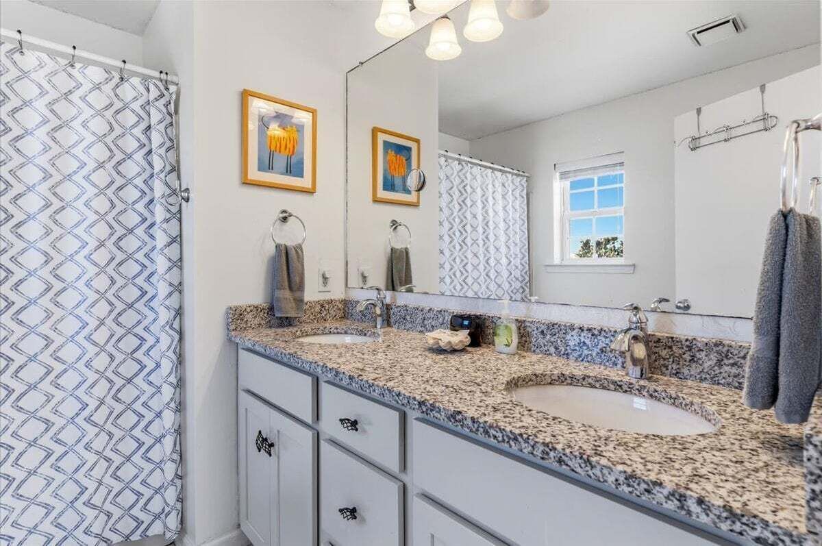 Une salle de bain avec deux lavabos, un grand miroir et un rideau de douche.
