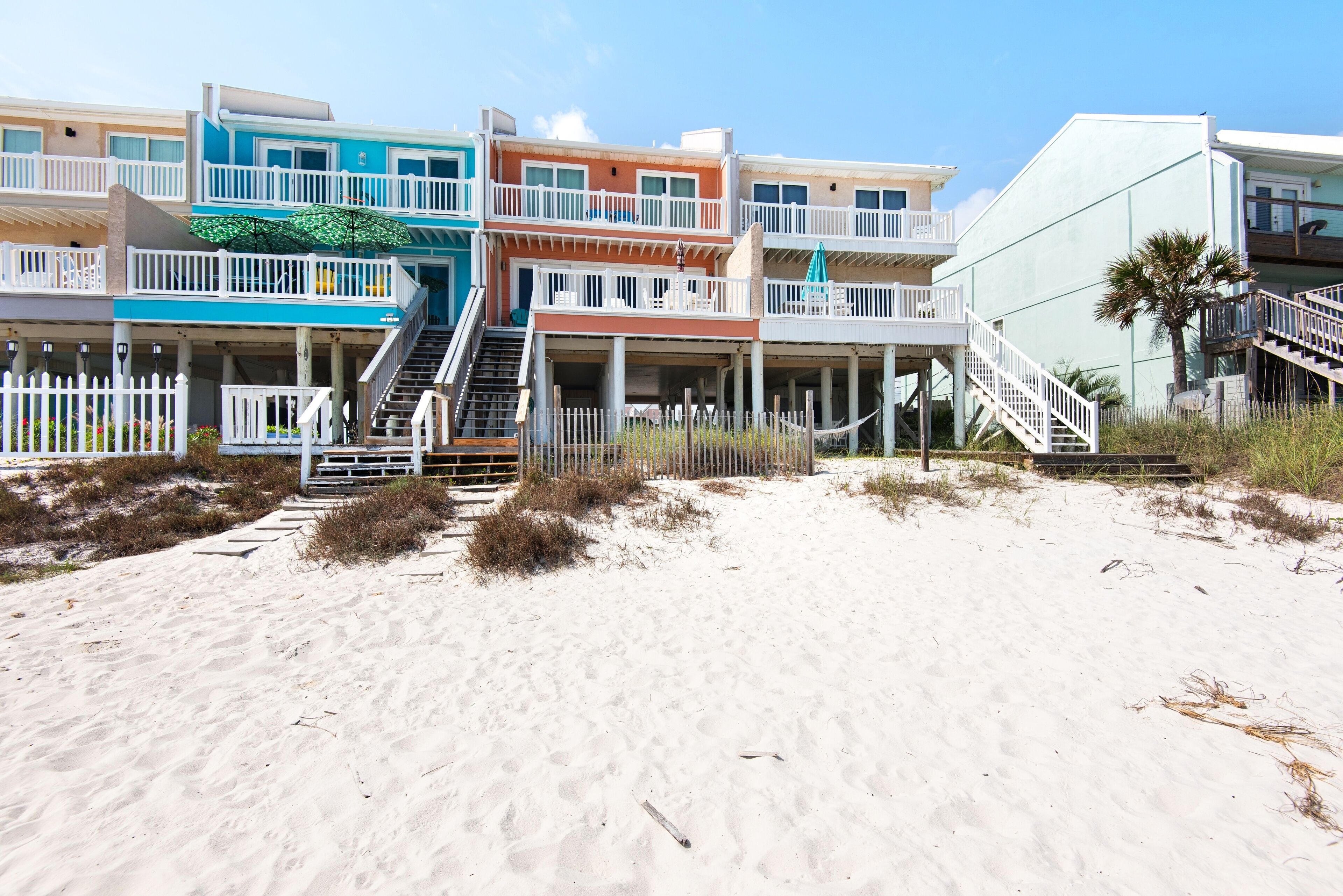 A beachfront property with multiple balconies, a sandy beach in front, and a staircase leading to the beach.