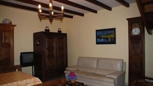 A cozy living room with a wooden ceiling, a beige sofa, a wooden cabinet, a small table with a vase, and a clock on the wall.