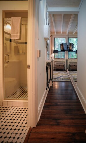 Un baño con cabina de ducha de vidrio, inodoro y lavabo. El suelo es de madera y el respaldas del lavabo tiene azulejos estampados.