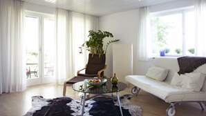 A modern living room with a glass coffee table, a white sofa, and a large window with curtains. - House on Schlossberg (Tuebingen)