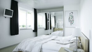 A hotel room with a bed, a bedside table with a lamp, a TV, and a large window with curtains. - House on Schlossberg (Tuebingen)
