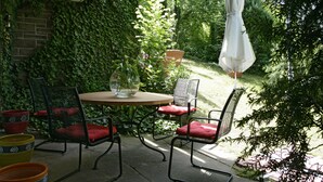 An outdoor patio with a round table and two chairs, surrounded by lush greenery and a brick wall. - House on Schlossberg (Tuebingen)