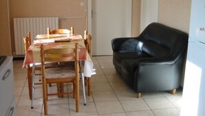 Ein Essbereich mit einem für vier Personen gedeckten Tisch, einem schwarzen Ledersessel und einem weißen Kühlschrank im Hintergrund.