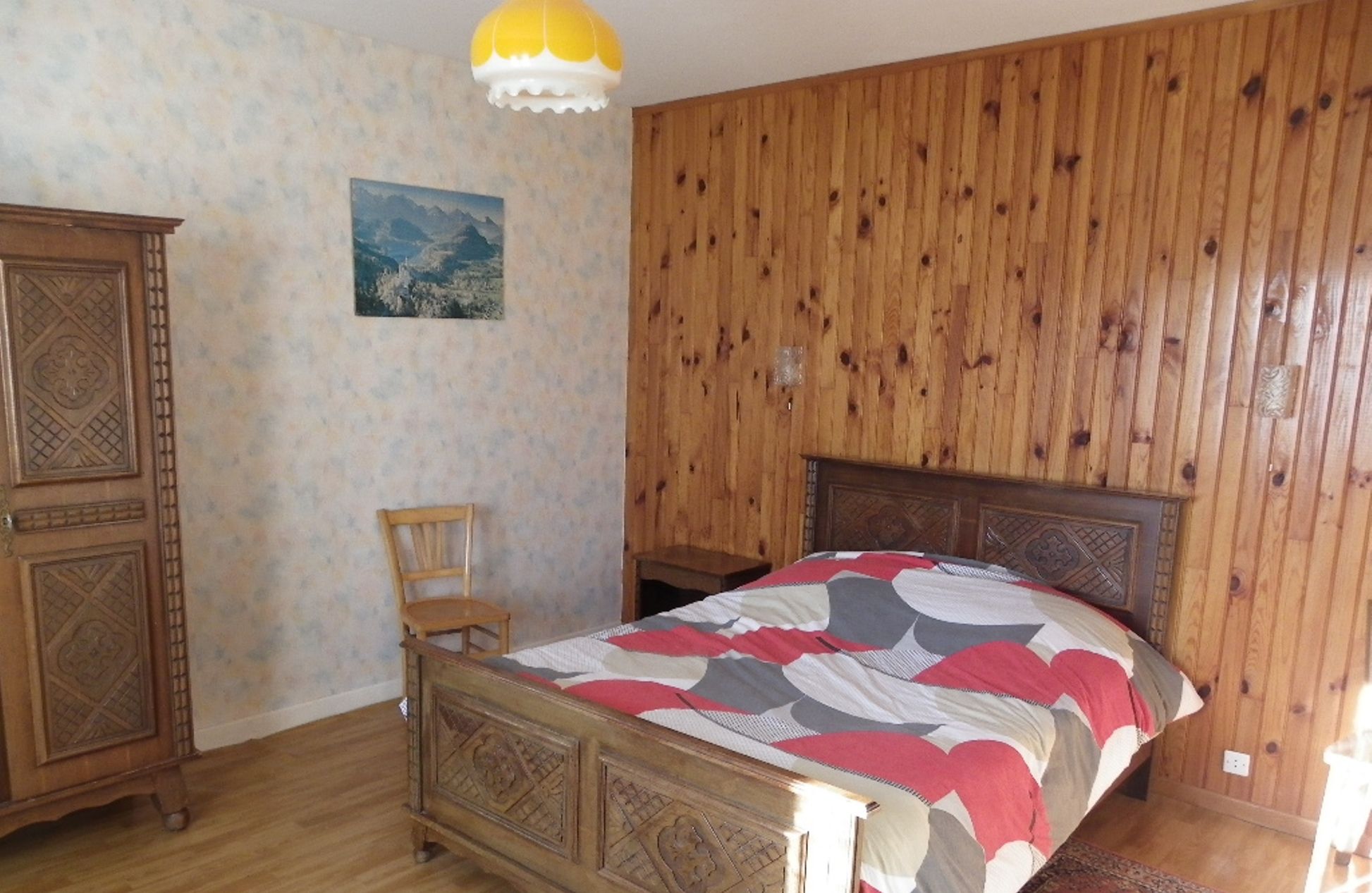 Un dormitorio con una cama y un armario de madera, una silla y un cuadro en la pared.