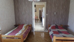 A room with two wooden beds, a herringbone-patterned wooden floor, and a door leading to a hallway.
