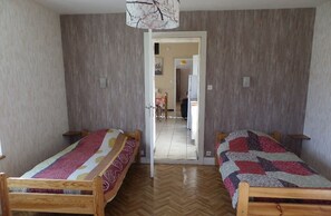 Une pièce avec deux lits en bois, un parquet en bois disposé en motif à chevrons et une porte donnant sur un couloir.