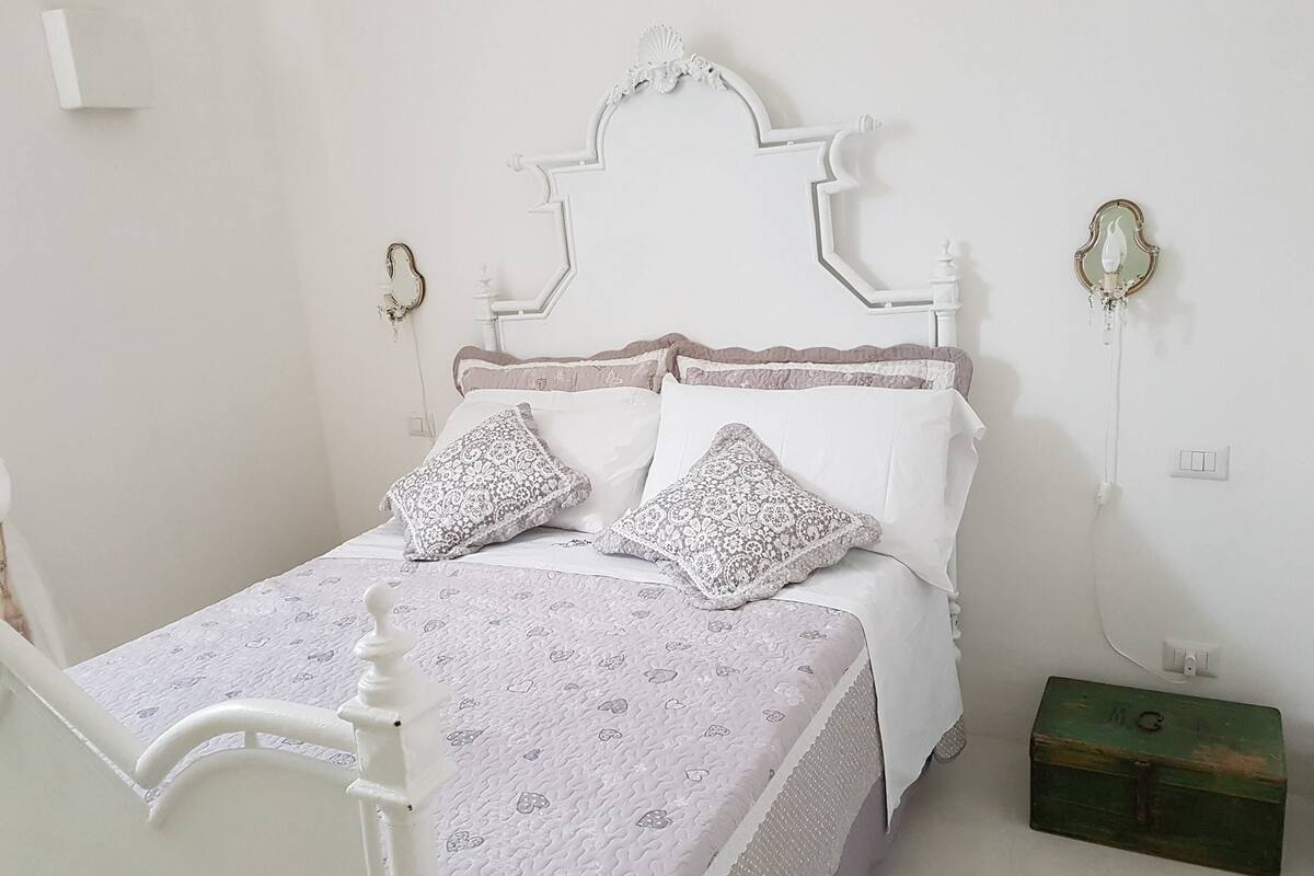 Un lit avec une tête de lit blanche, deux coussins à motifs et une table de chevet blanche.