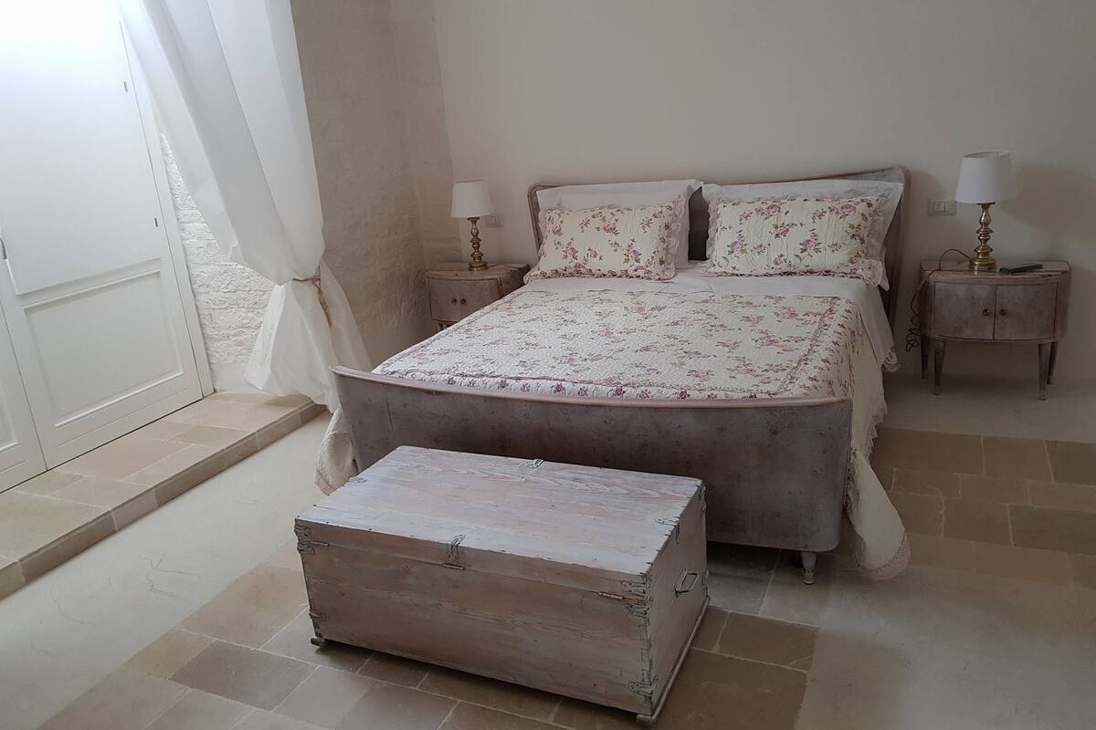 Une chambre à coucher comprenant un lit, deux tables de chevet, une commode, une commode à tiroirs et une fenêtre avec des rideaux.
