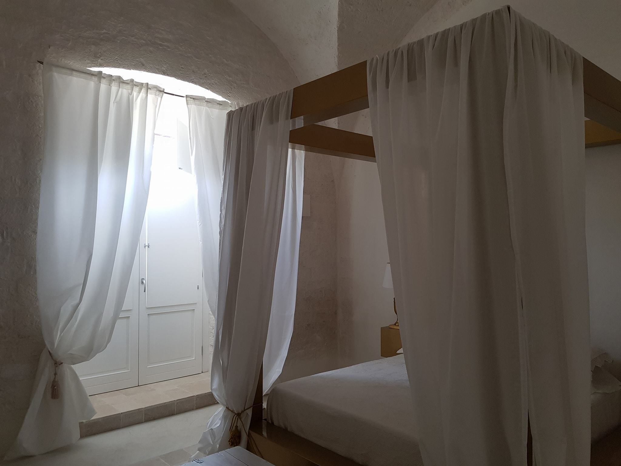 Une chambre avec un lit simple, des rideaux blancs et une fenêtre donnant sur un beau paysage.