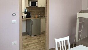 A compact room with a kitchenette, a TV mounted above the counter, and a small dining table with a chair. - B&B Arco dolce Arco (Benevento)