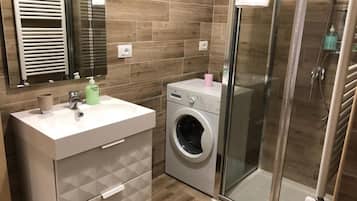 A modern bathroom with a built-in washing machine, a glass shower enclosure, and a vanity with a mirror.