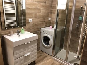 Un baño moderno con lavadora integrada, cabina de ducha de cristal y tocador con espejo.