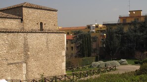 Un edificio de piedra con techo de tejas, rodeado de edificios modernos y vegetación.