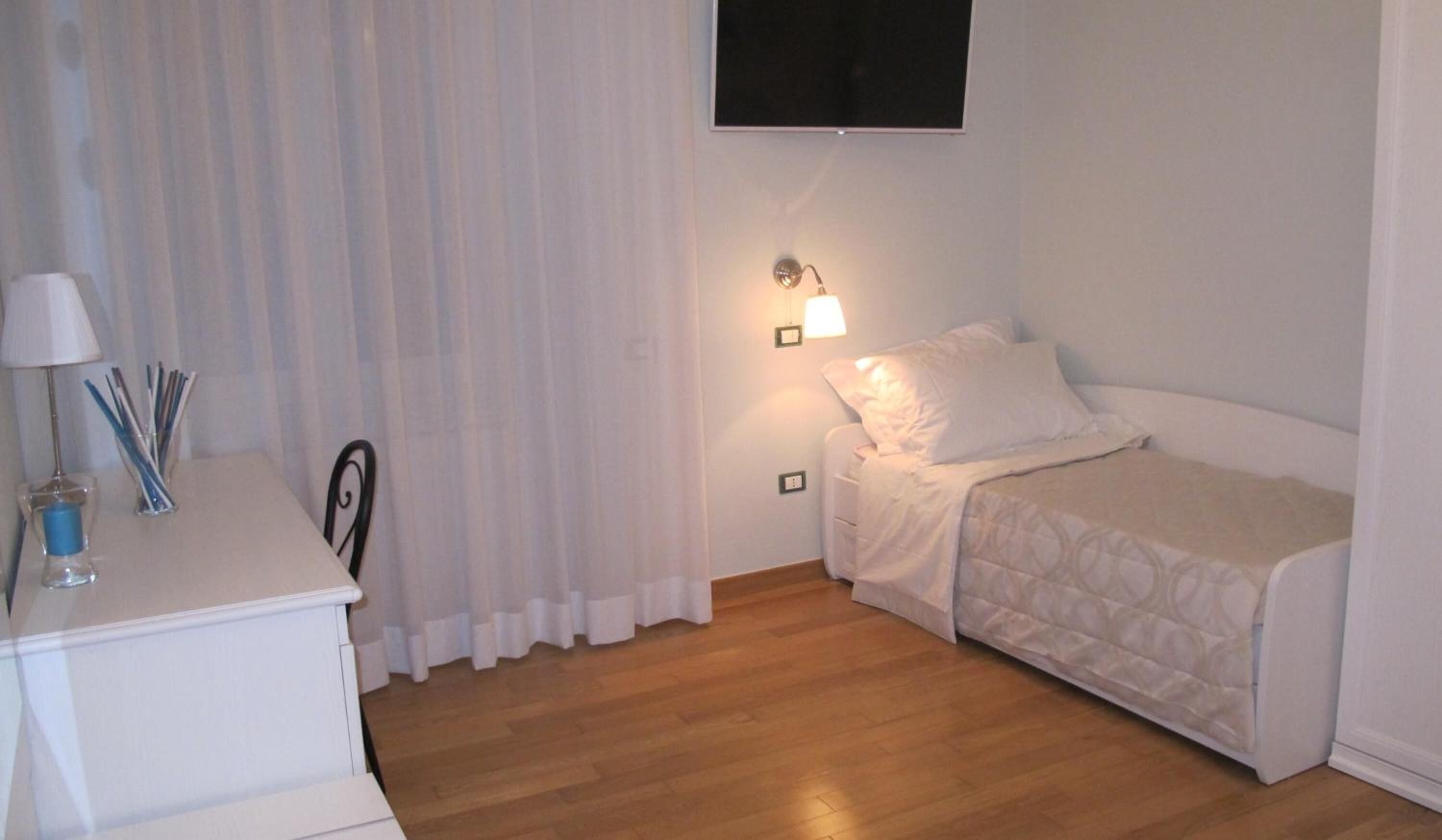 A small, neatly arranged bedroom with a single bed, a bedside table with a lamp, and a chair.