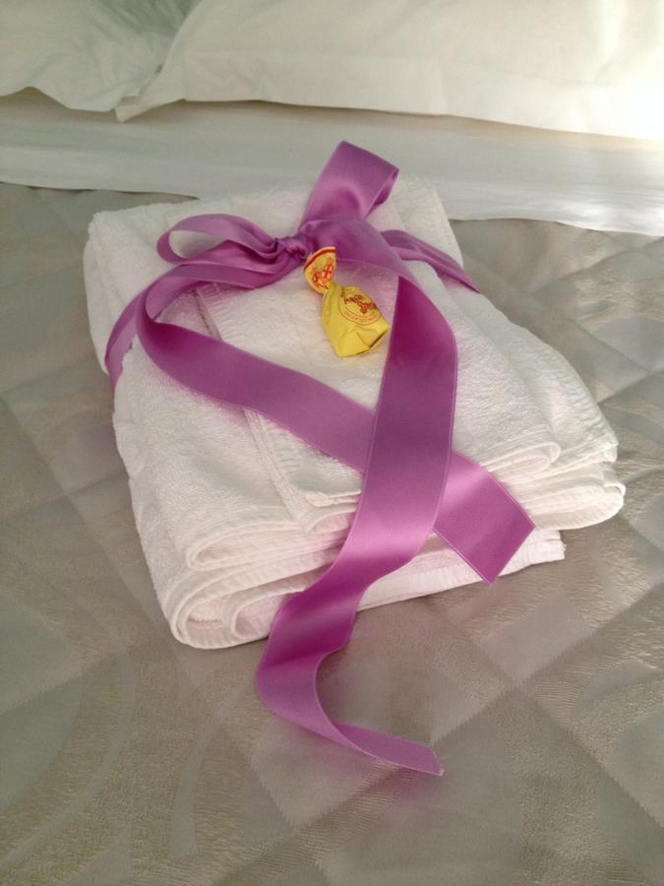 Une pile de serviettes blanches, soigneusement pliées et maintenue par un ruban violet, est posée sur une surface texturée.