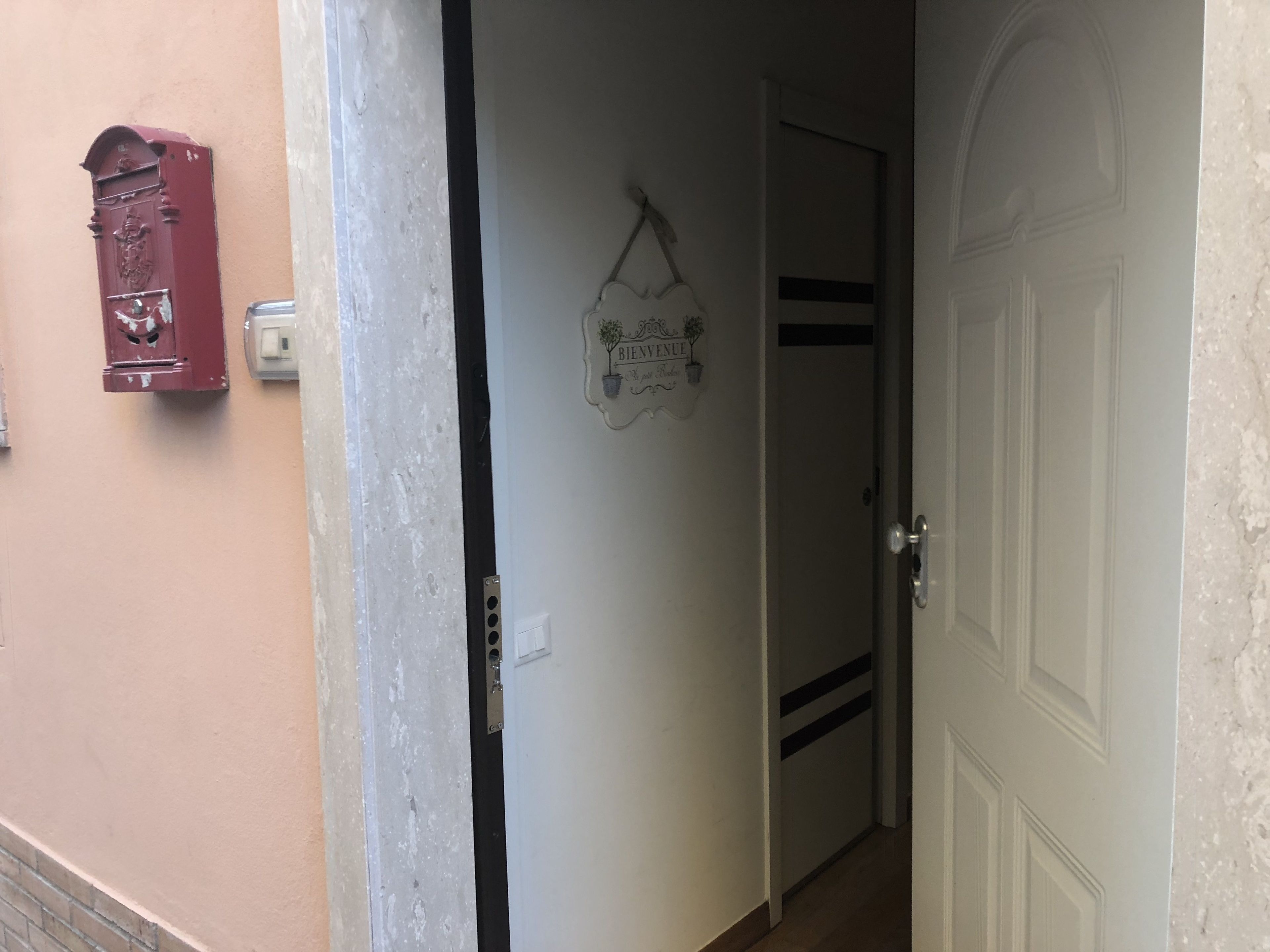 Ein Flur mit einer Tür, auf der “BENVENUE” steht, und einem Briefkasten an der Wand.
