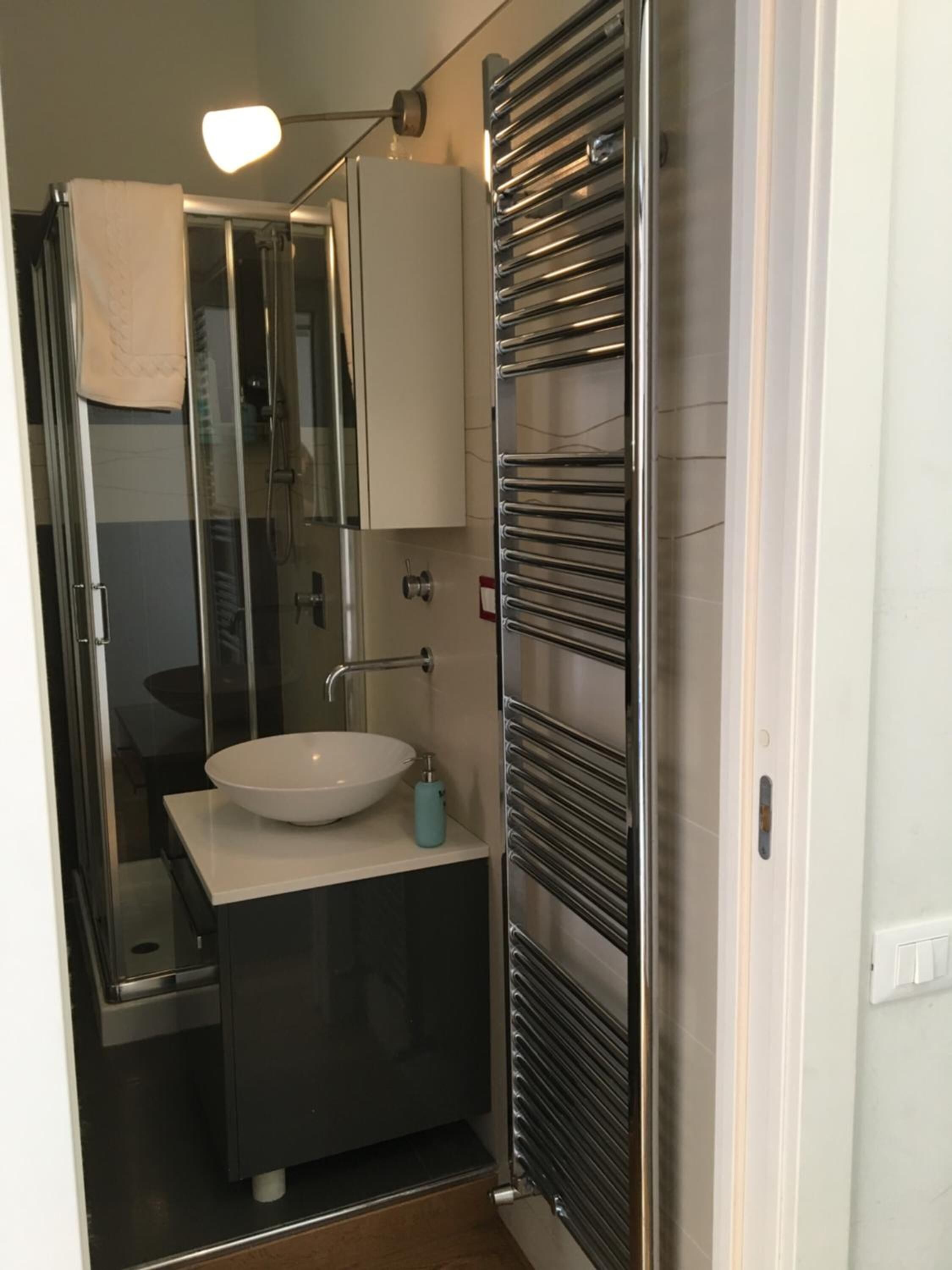 Un bany modern amb una dutxa de vidre, un lavabo blanc i una barra de tovalloles.