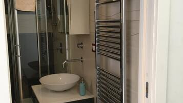 Un baño moderno con cabina de ducha de vidrio, un lavabo blanco y un perchero para toallas.