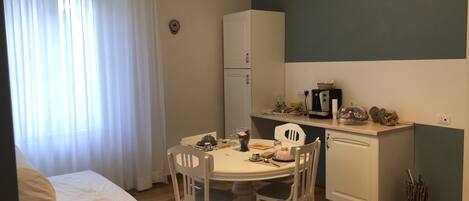 A compact kitchen with a dining table, chairs, a refrigerator, and a coffee maker.