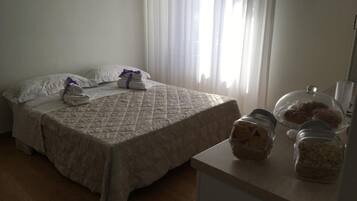 Habitación de hotel con una cama, una pequeña mesa con pasteles y un ventanal con cortinas.