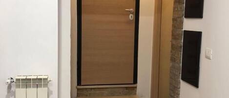 Un couloir avec une porte en bois, un radiateur et un mur d’accent en pierre.