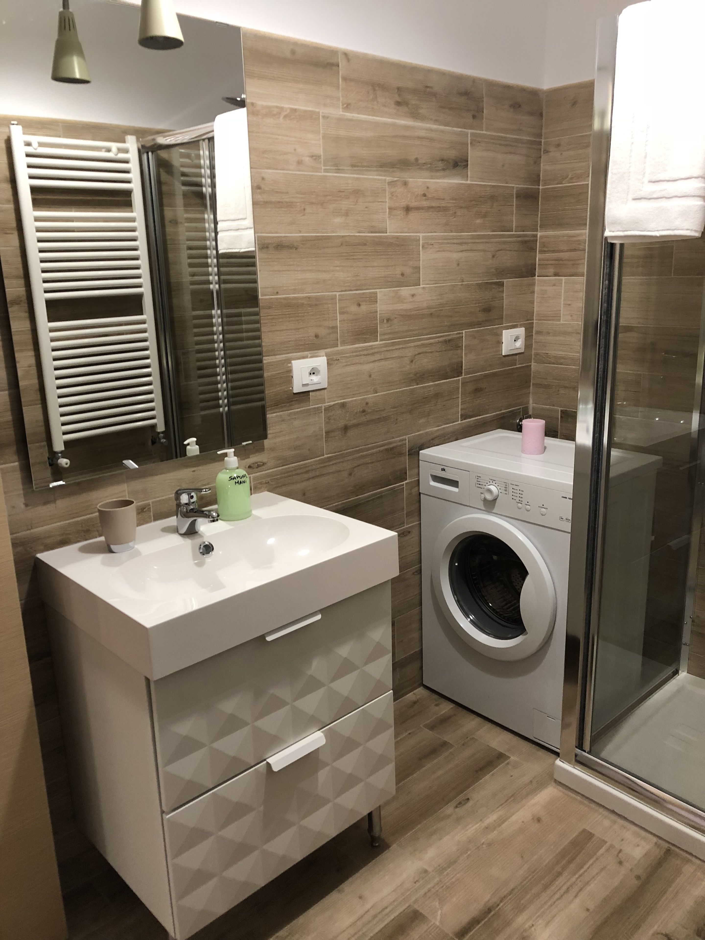 A modern bathroom with a built-in washing machine, a vanity with a mirror, and a shower area.