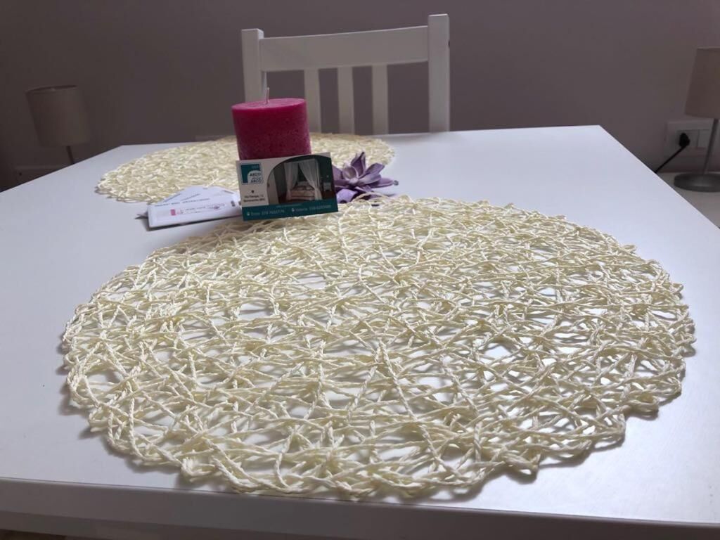 Una mesa con mantel blanco, una vela rosa, una caja de pañuelos y un pequeño marco de fotos.