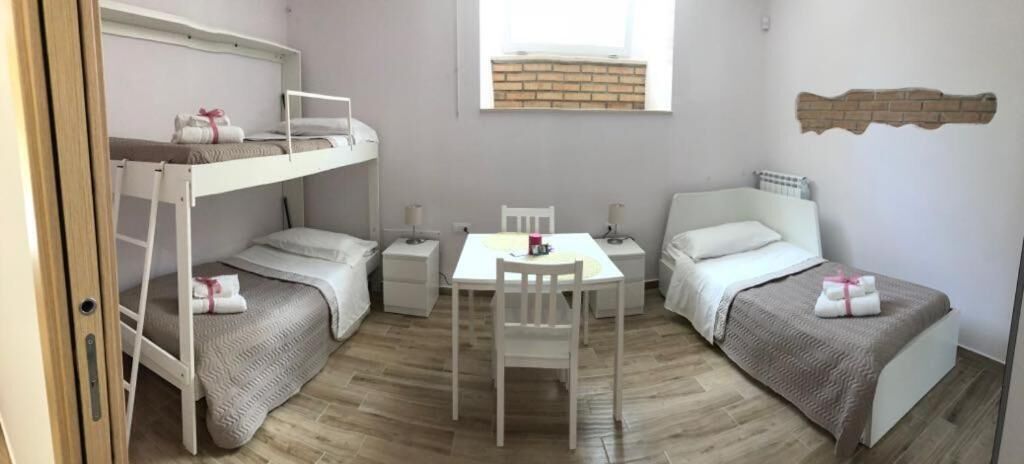 Une chambre avec des lits superposés, une petite table, deux tables de chevet et une fenêtre donnant sur un mur de briques.