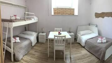 Une chambre avec des lits superposés, une petite table, deux tables de chevet et une fenêtre donnant sur un mur de briques.