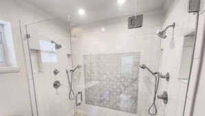 Une douche fermée par des parois de verre, avec un mur recouvert de carreaux décoratifs, des toilettes et un lavabo.