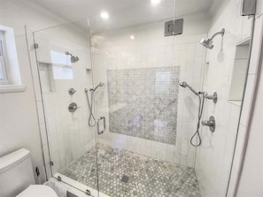 Um chuveiro com paredes de vidro, azulejos estampados, vaso sanitário e pia.