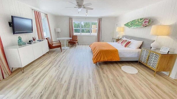Une chambre d’hôtel équipée d’un lit, d’un bureau, d’une chaise, d’une télévision, d’un ventilateur de plafond et d’une fenêtre.