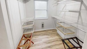 Une pièce de rangement avec des étagères blanches, une échelle en bois et une fenêtre.