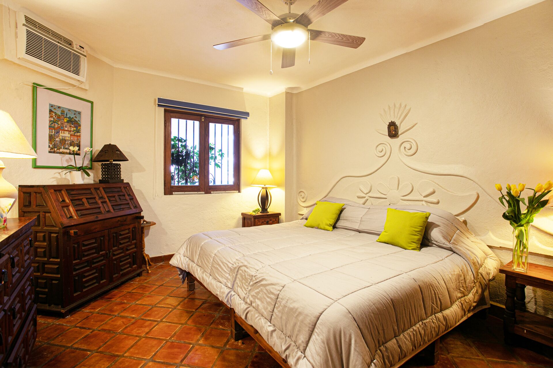 Une chambre à coucher comprenant un lit, un ventilateur de plafond, une fenêtre et un climatiseur fixé au mur.