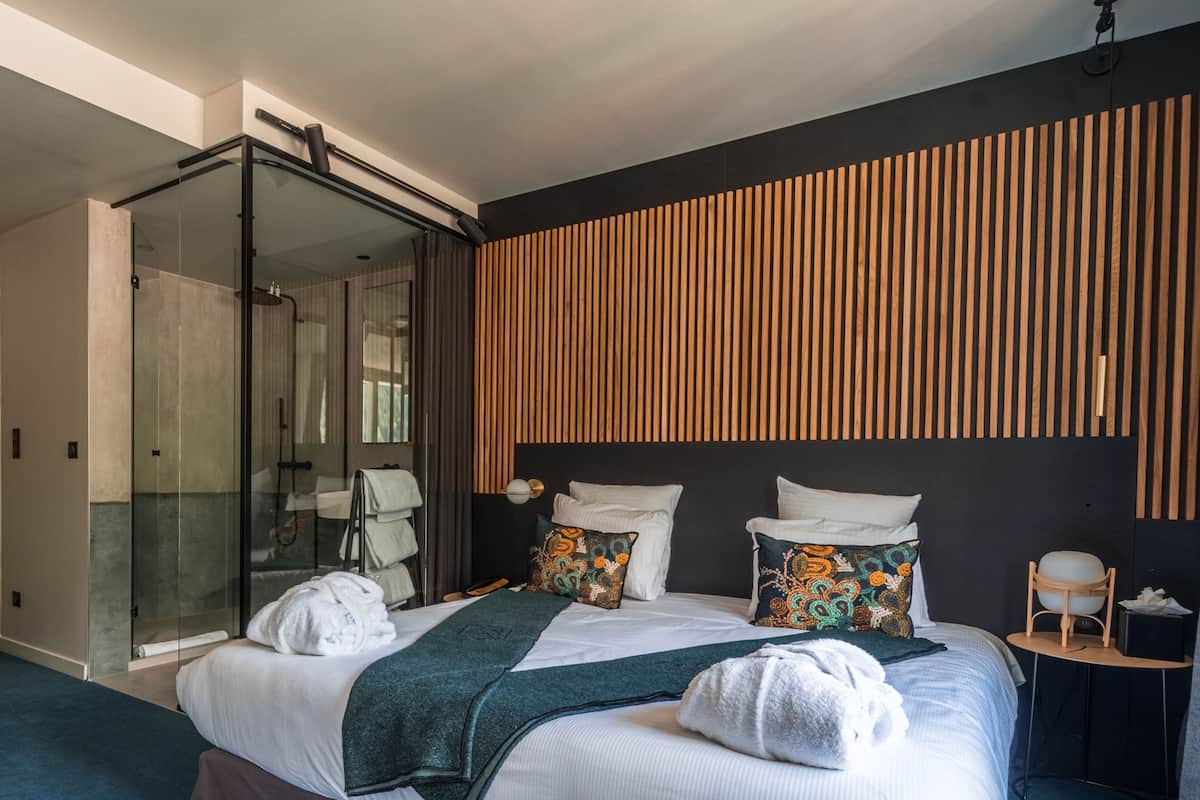 Une chambre d’hôtel moderne dotée d’une douche en verre, d’un lit avec de nombreux oreillers et d’un mur en lambris de bois.