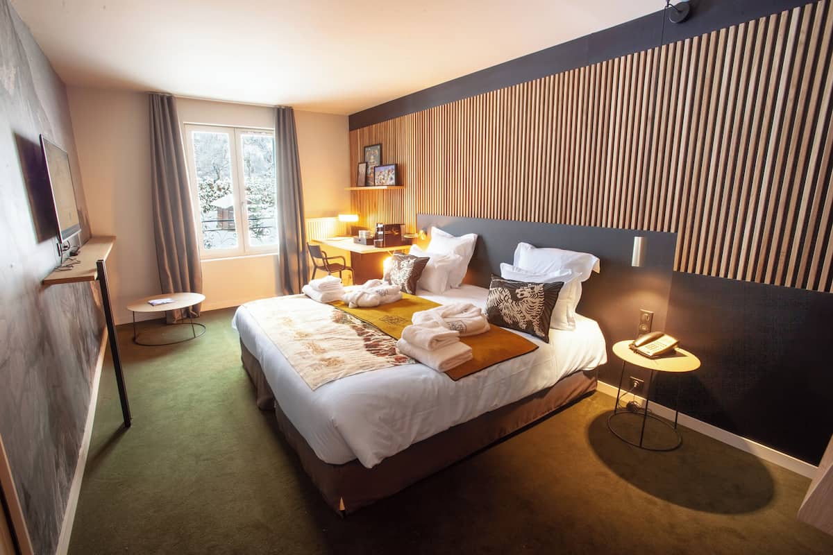 Une chambre d’hôtel avec un grand lit, un bureau, une chaise, une petite table, un téléviseur et une fenêtre avec des rideaux.